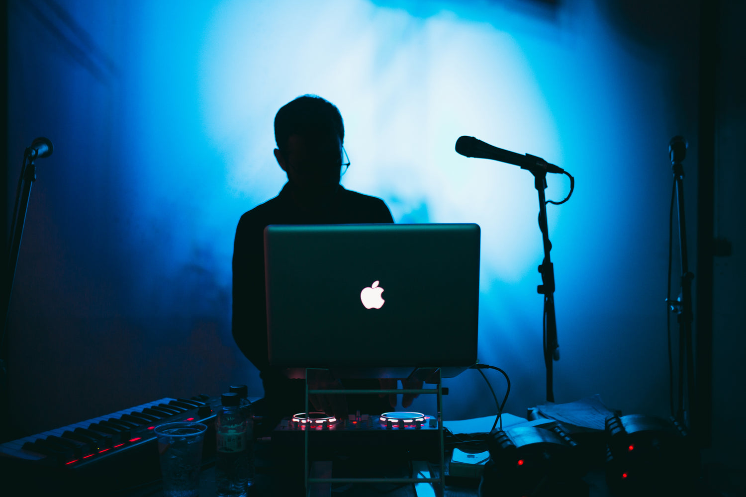 DJ silhouetted behind laptop and microphones - how to change lyrics with AI