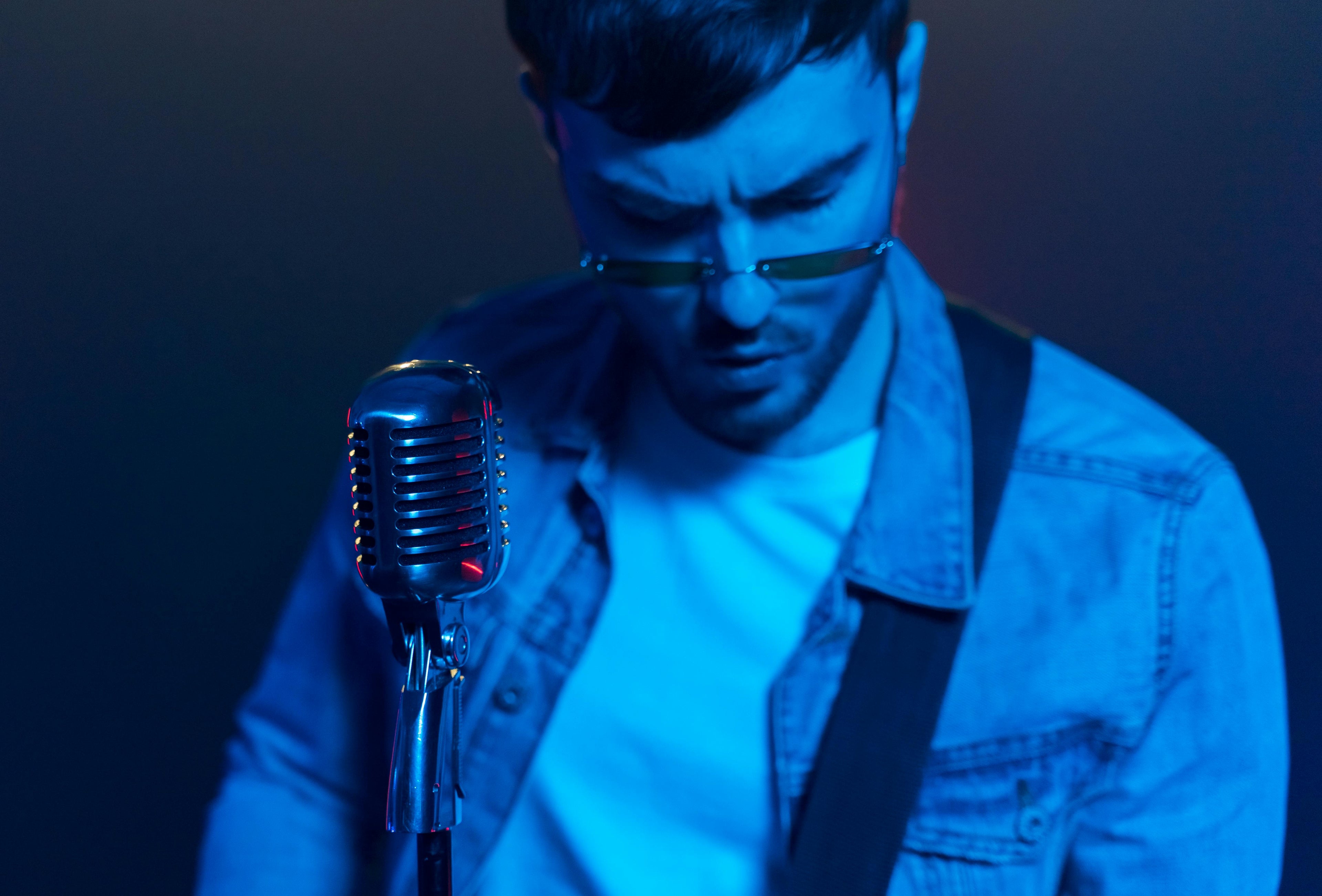 Male singer in blue lighting performing with vintage microphone – song lyric changer concept